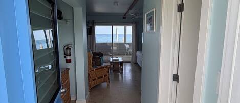 A hallway leading to a living area with a view of the sea, a ceiling fan, and a fire extinguisher.