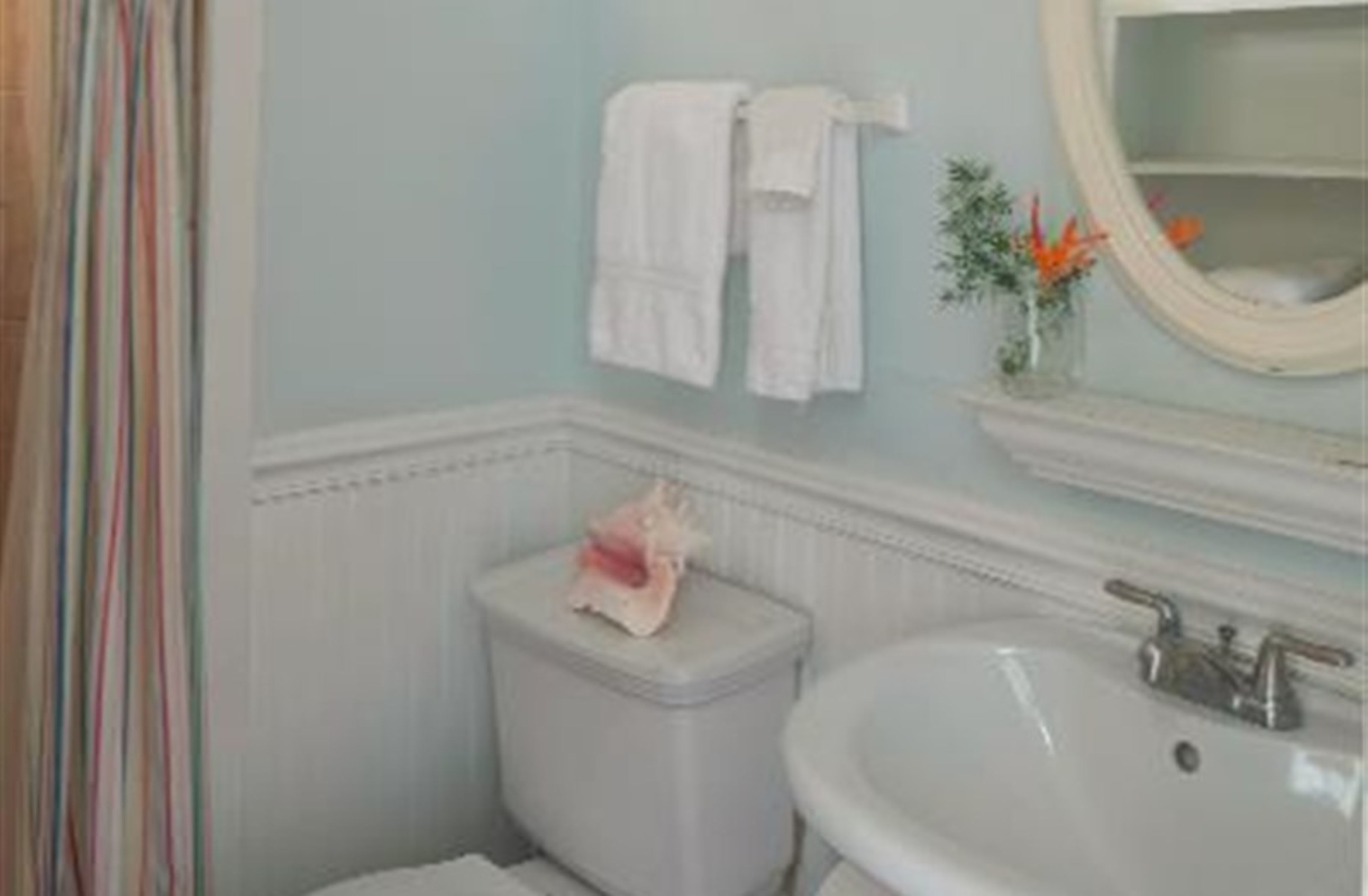 A bathroom with a toilet, sink, and a mirror. There are towels hanging on the wall and a small vase with flowers.
