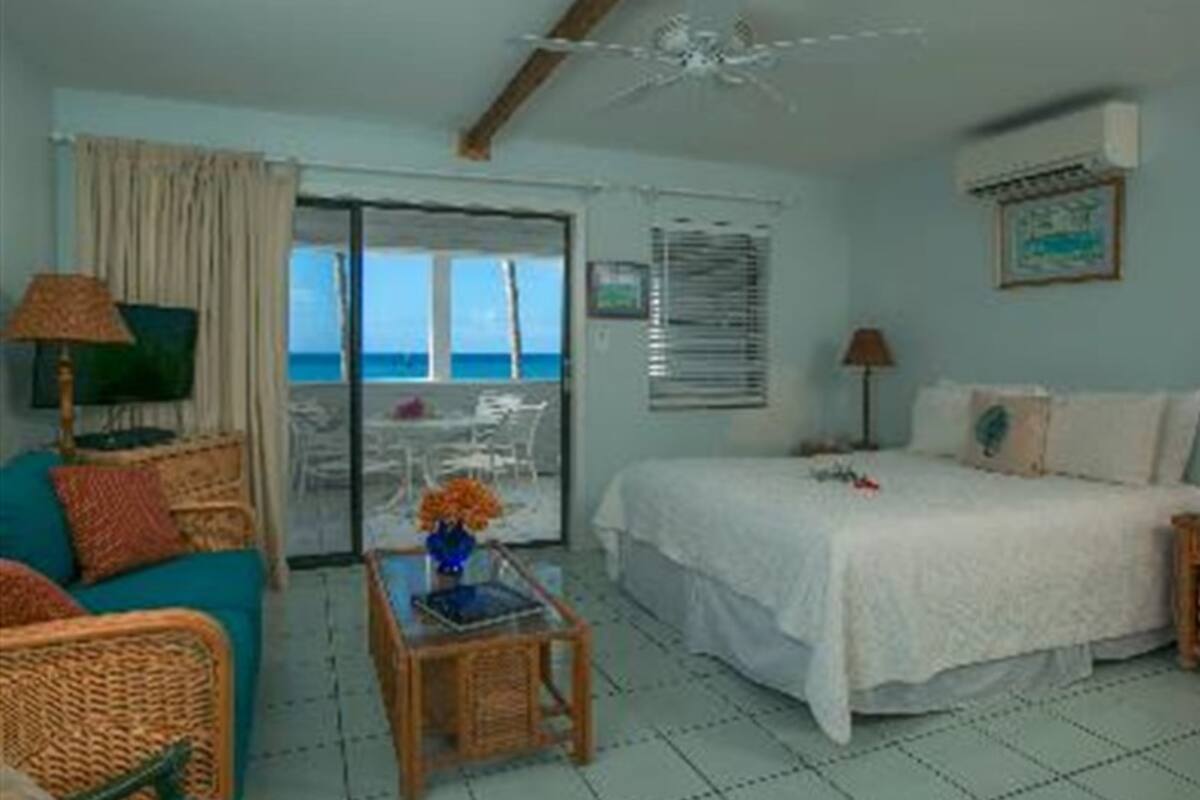 A room with a bed, a chair, a table with a vase, and a view of the sea through a glass door.