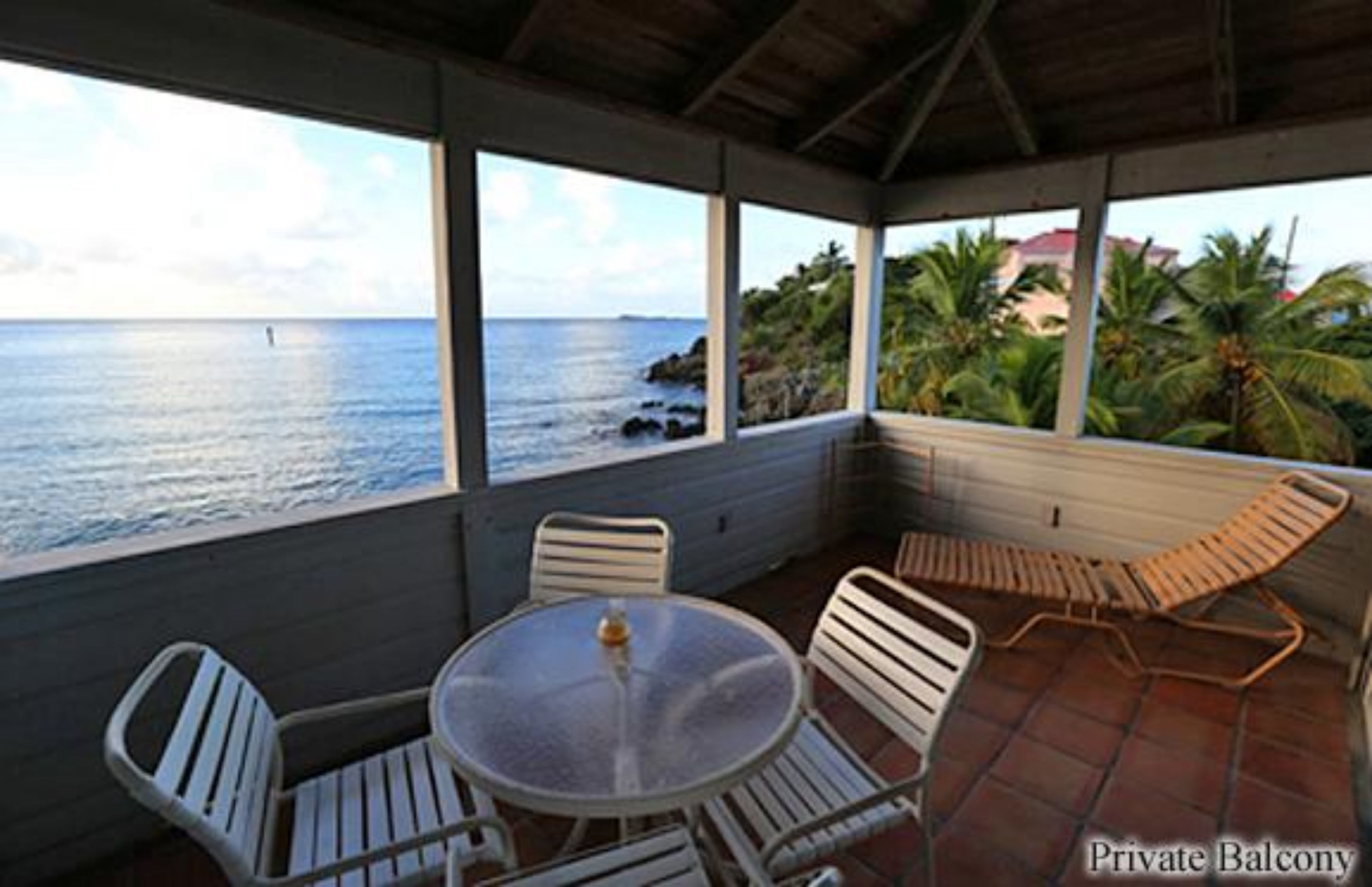 Un área de estar al aire libre con techo, una mesa y sillas, con vista al mar y un paisaje tropical.