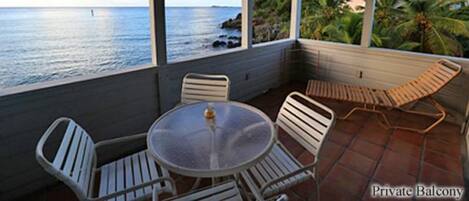 Un área de estar al aire libre con techo, una mesa y sillas, con vista al mar y un paisaje tropical.