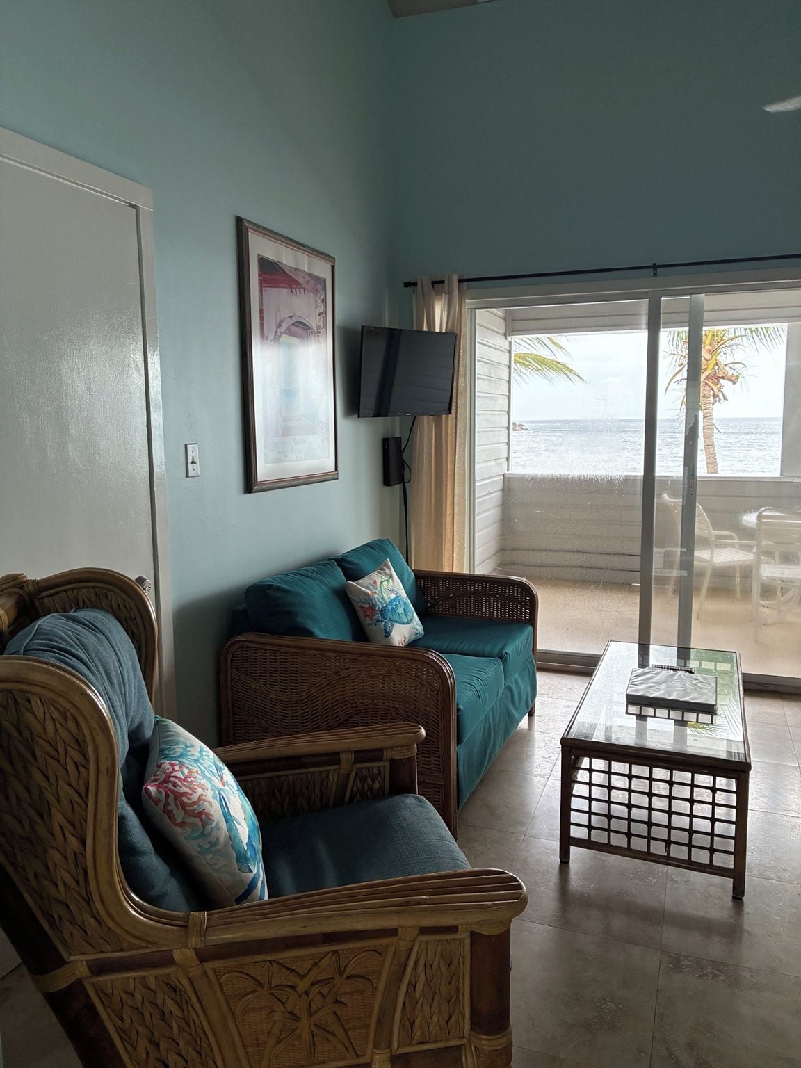 A living room with a sofa, a television, and a view of the beach.