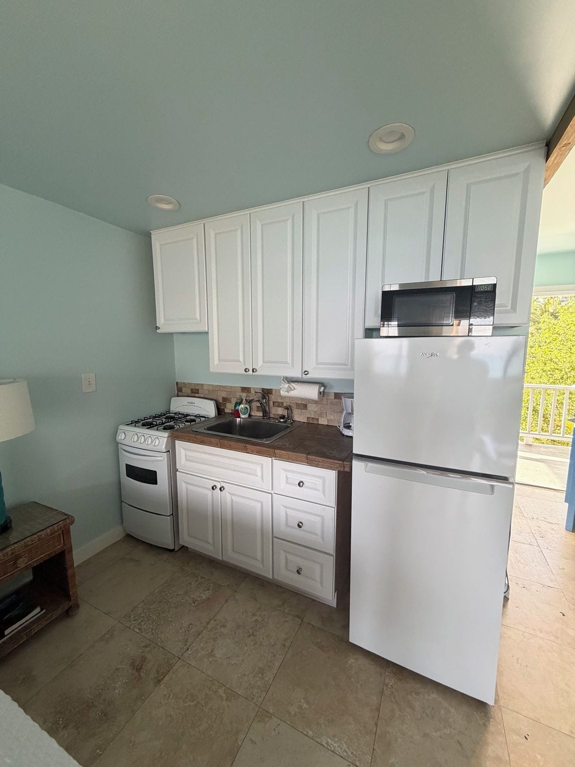 A compact kitchen with white cabinets, a stove, a sink, and a refrigerator.
