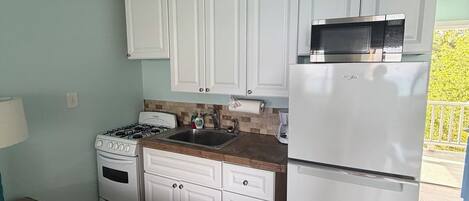 A compact kitchen with white cabinets, a stove, a sink, and a refrigerator.
