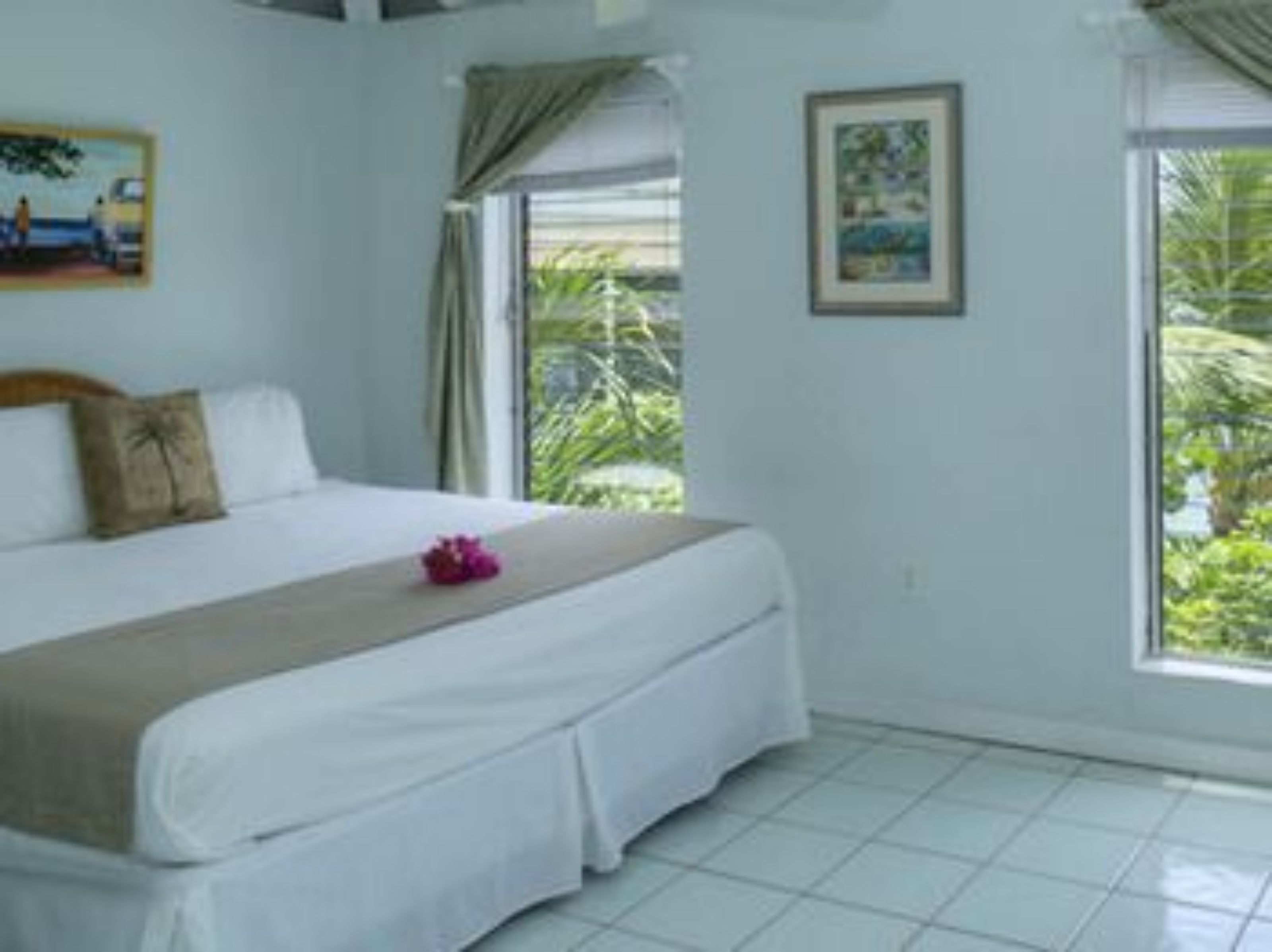 A hotel room with a bed, a window with curtains, and a painting on the wall.