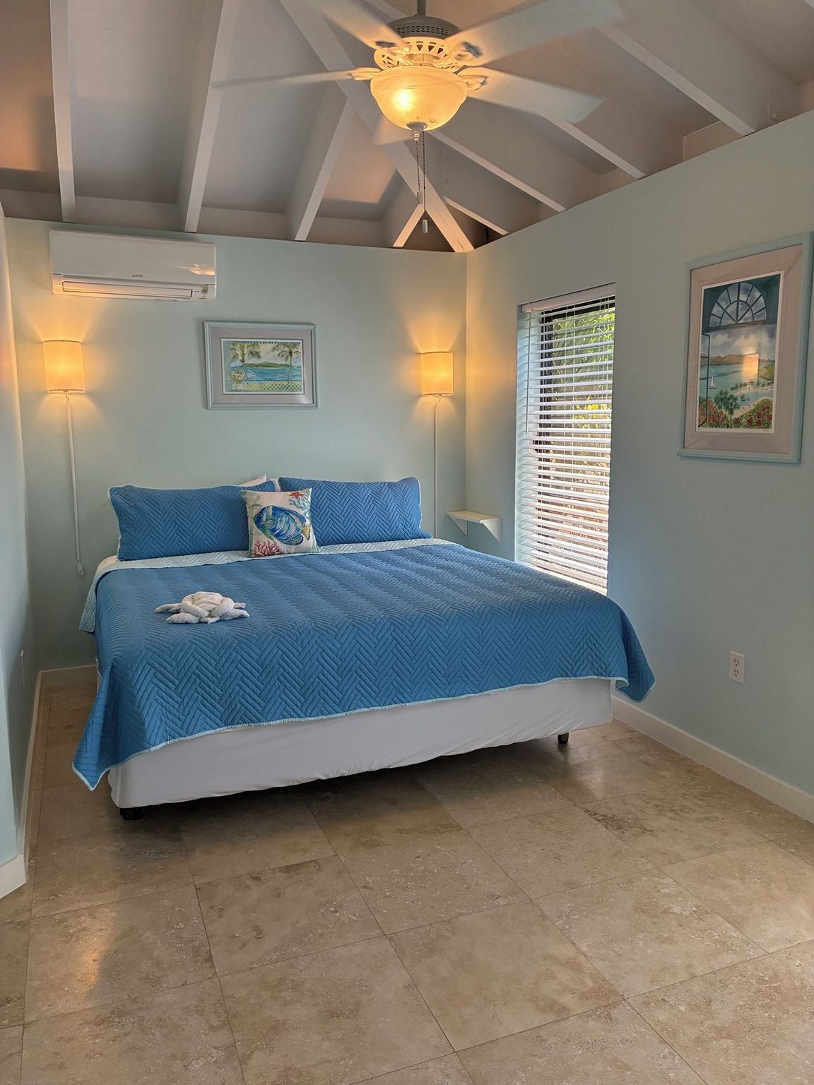 A bedroom with a bed, two wall-mounted lamps, a ceiling fan, and a window with blinds.
