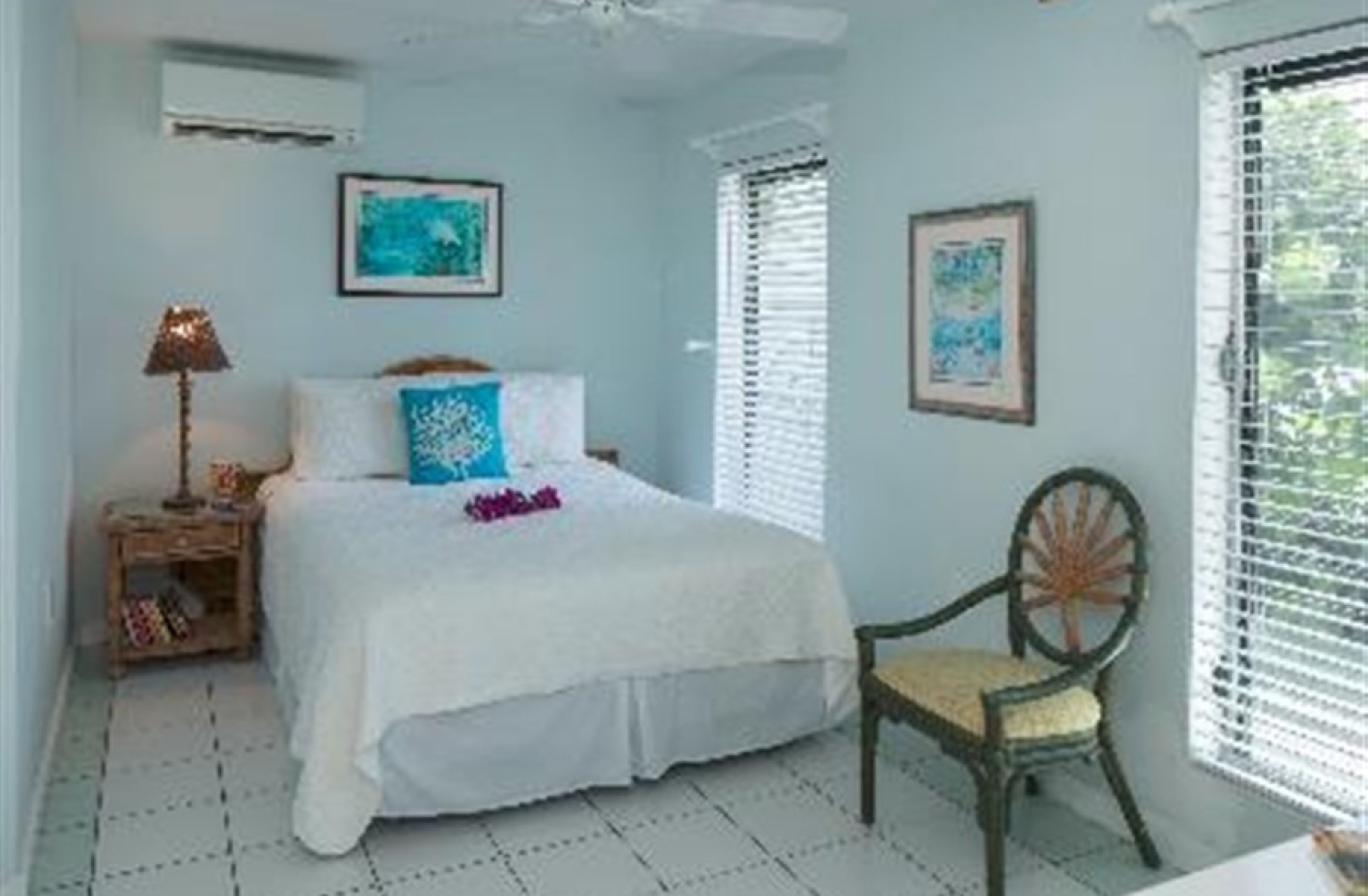 A bedroom with a bed, a chair, a nightstand, and two framed pictures on the wall.