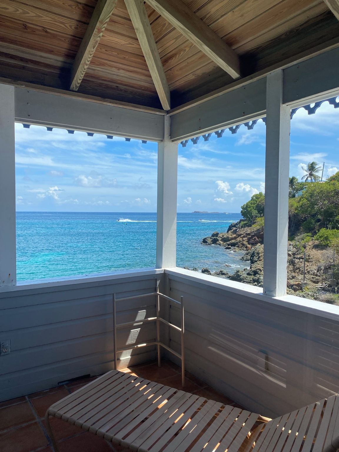 A covered outdoor seating area with a view of the ocean and a rocky shoreline.