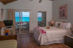 Une chambre à coucher avec un lit, une télévision, un bureau et un balcon donnant sur l’océan.