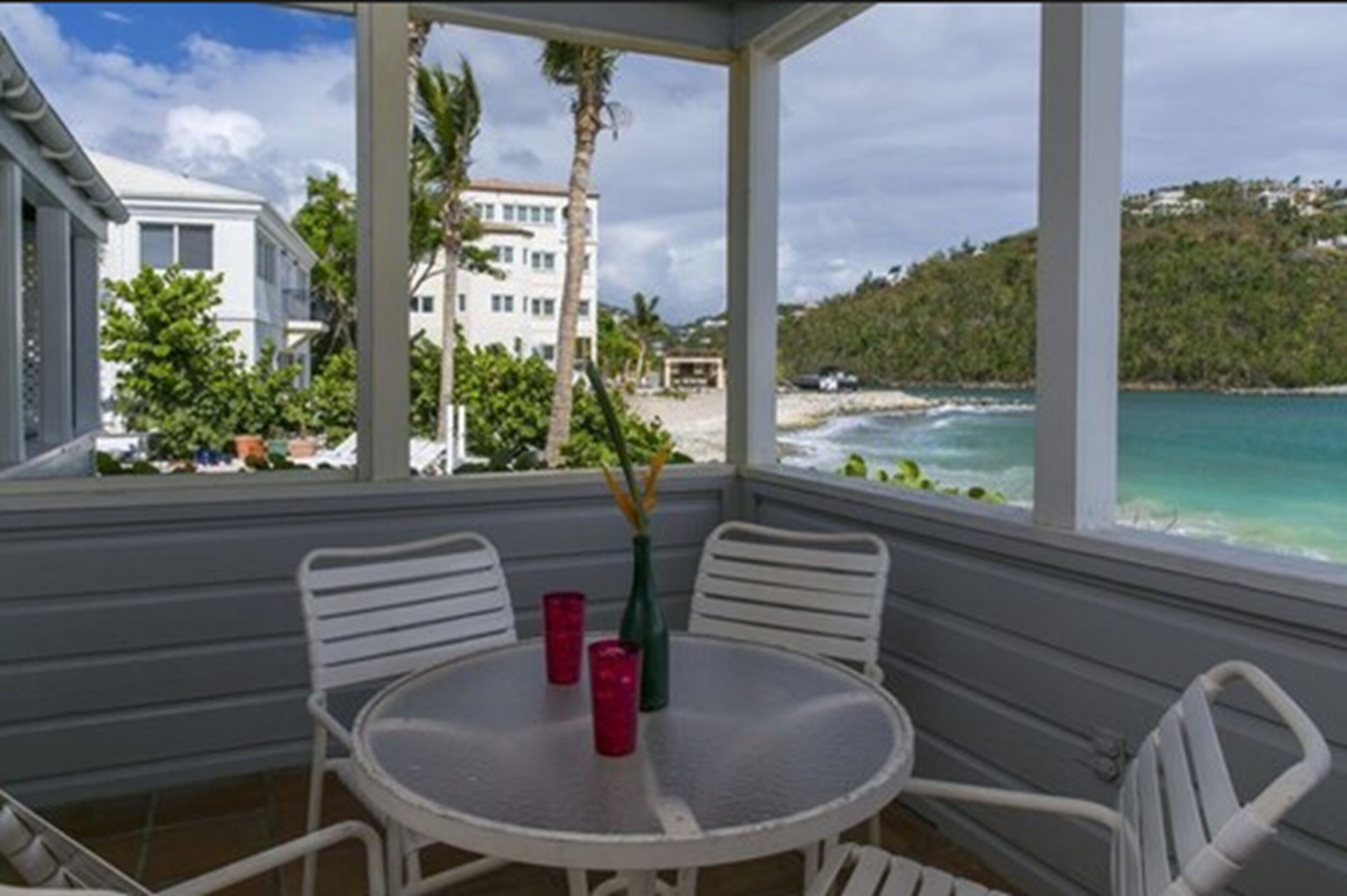 Ein überdachter Sitzbereich im Freien mit Tisch und Stühlen, mit Blick auf Strand und Meer.