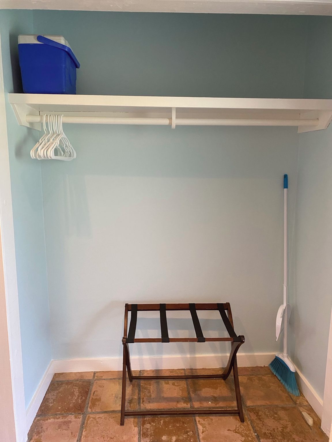 Ein Zimmer mit einem weißen Regal, einem blauen Behälter, einem weißen Kleiderständer und einem Besen.