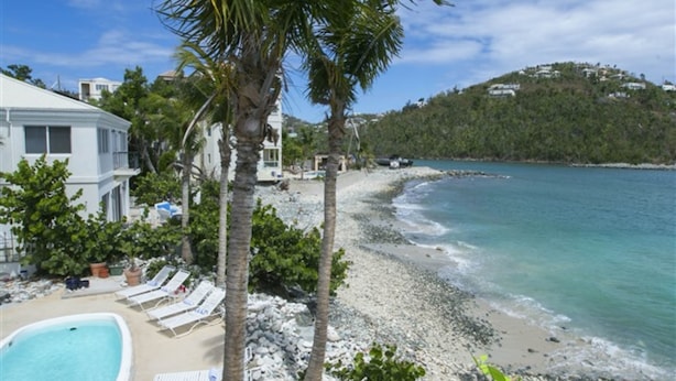 A beachfront property with a swimming pool, lounge chairs, and a view of the sea. - Coconut Coast Villas (St. John)