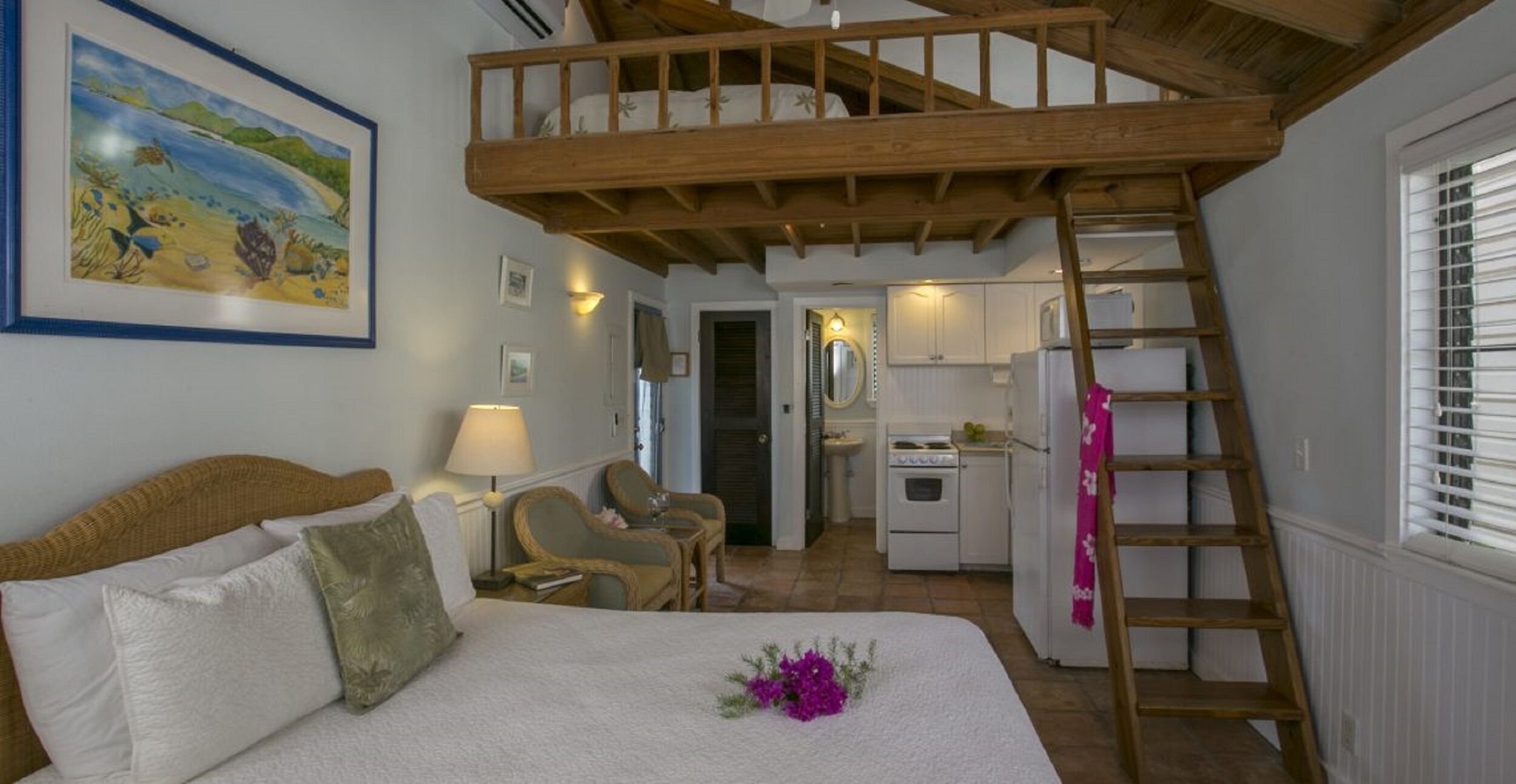 Een slaapkamer met een stapelbed, een bureau, een stoel, een nachtkastje, een lamp en een schilderij aan de muur.