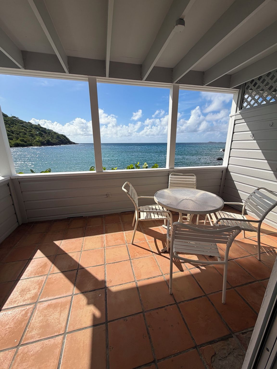 A covered patio with a table and chairs, overlooking a body of water and a distant landmass.