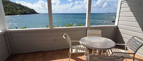 A covered patio with a table and chairs, overlooking a body of water and a distant landmass.