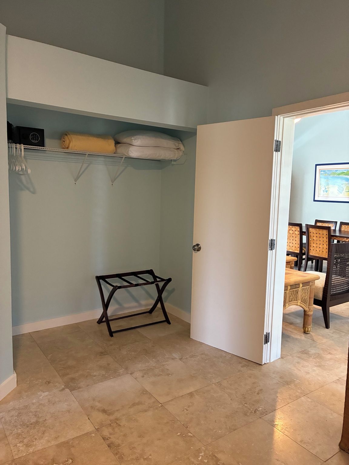 A room with a door leading to a dining area, a shelf with towels, and a drying rack.
