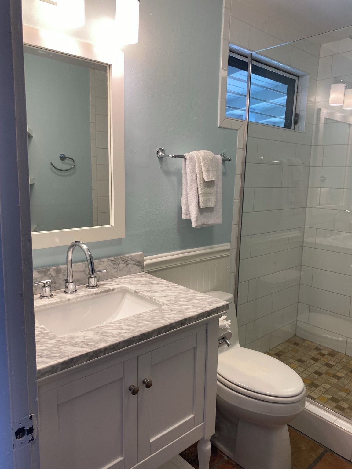 A bathroom with a white sink, a mirror, a towel rack, a toilet, and a glass shower enclosure.