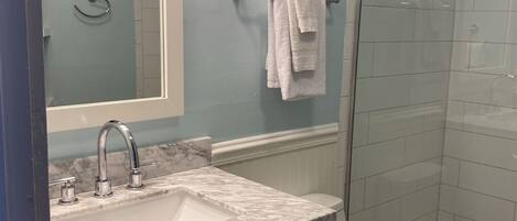 A bathroom with a white sink, a mirror, a towel rack, a toilet, and a glass shower enclosure.
