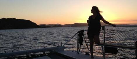 A person standing on a boat deck during sunset.