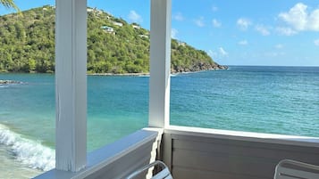 Un espace extérieur abrité, aménagé avec des sièges, offrant une vue sur la mer et une colline.