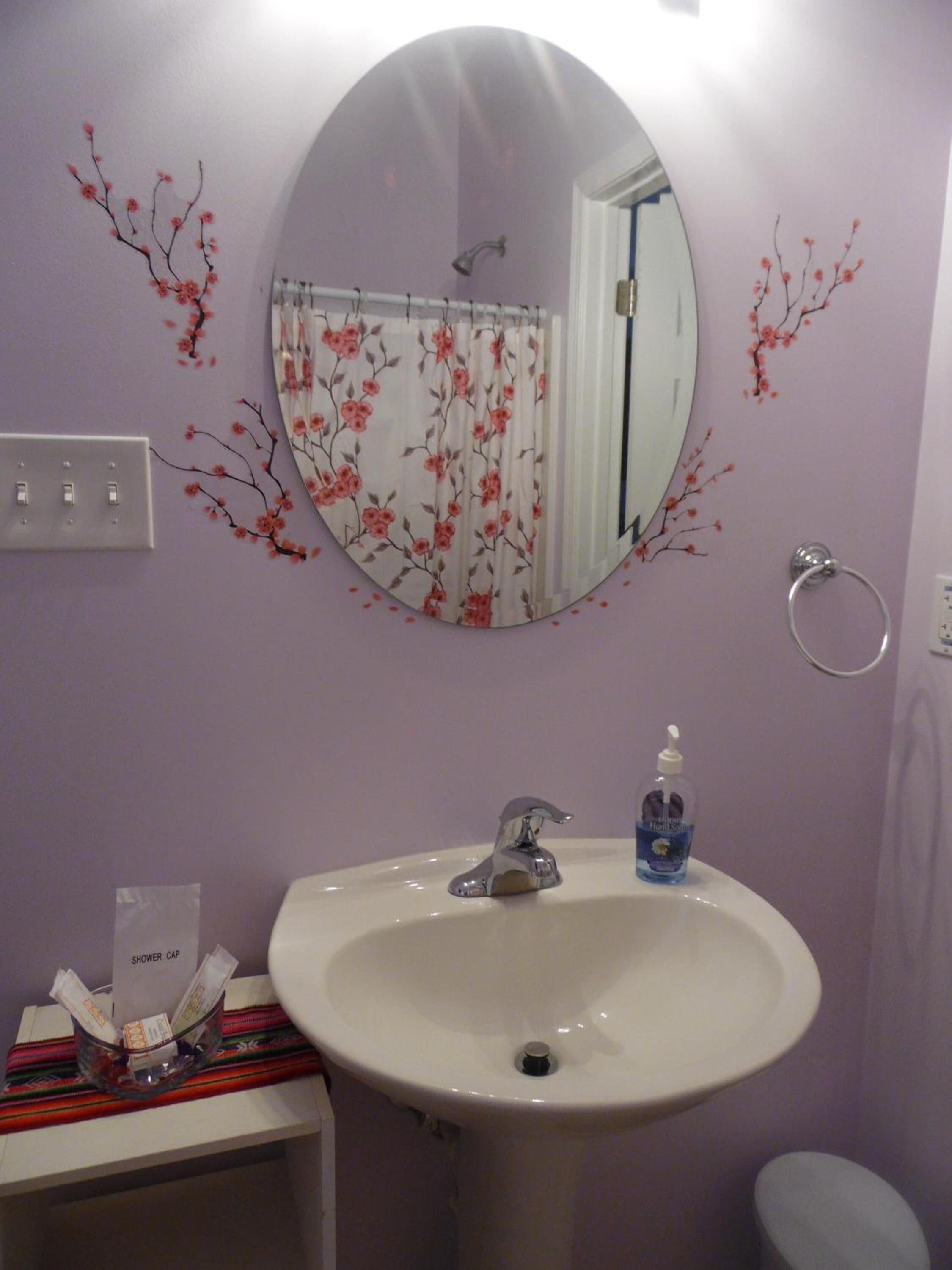 Un baño con un espejo redondo, un lavamanos blanco y una cortina de ducha con motivos florales.