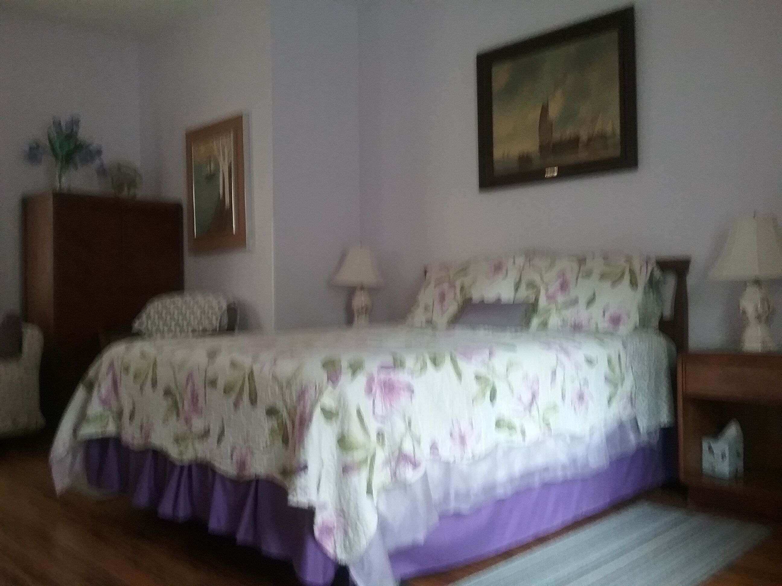Une chambre à coucher avec un lit, une commode, une lampe et un tableau au mur.