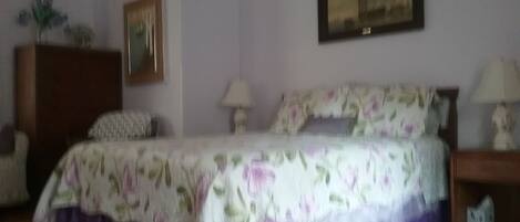 Une chambre à coucher avec un lit, une commode, une lampe et un tableau au mur.