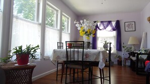 Un coin repas avec une table dressée pour deux personnes, un ventilateur de plafond et de grandes fenêtres avec des rideaux.