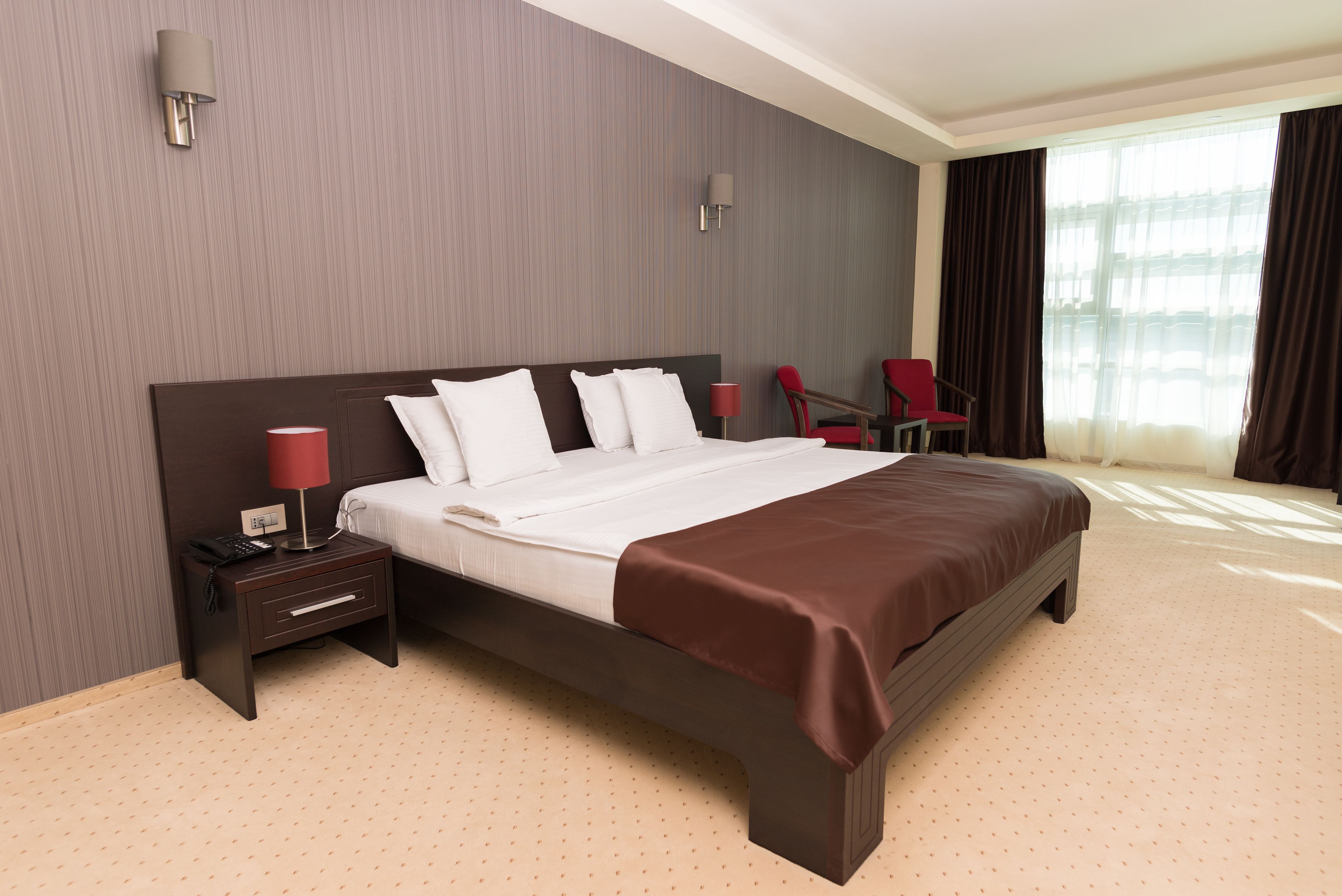 Ein Hotelzimmer mit einem großen Bett, einem Nachttisch mit Lampe, einem Sessel und einem Fenster mit Vorhängen.