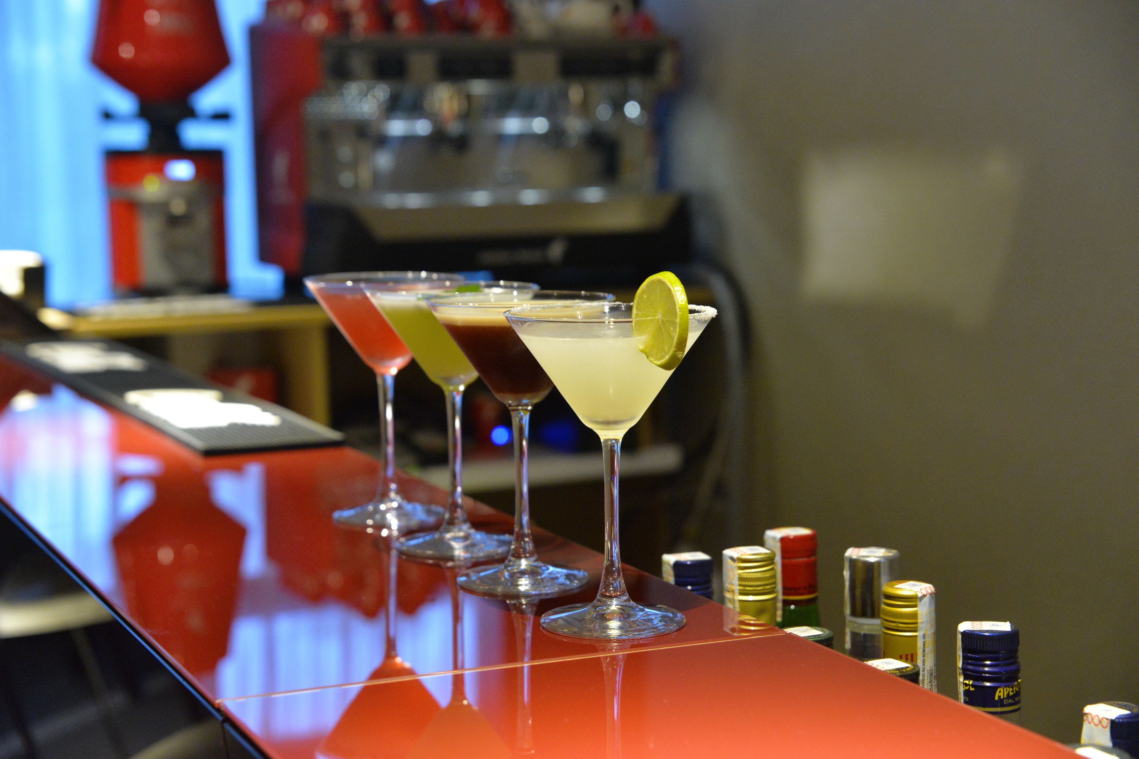 A bar with three martini glasses on a red bar counter, each with a different colored drink and a lime garnish.