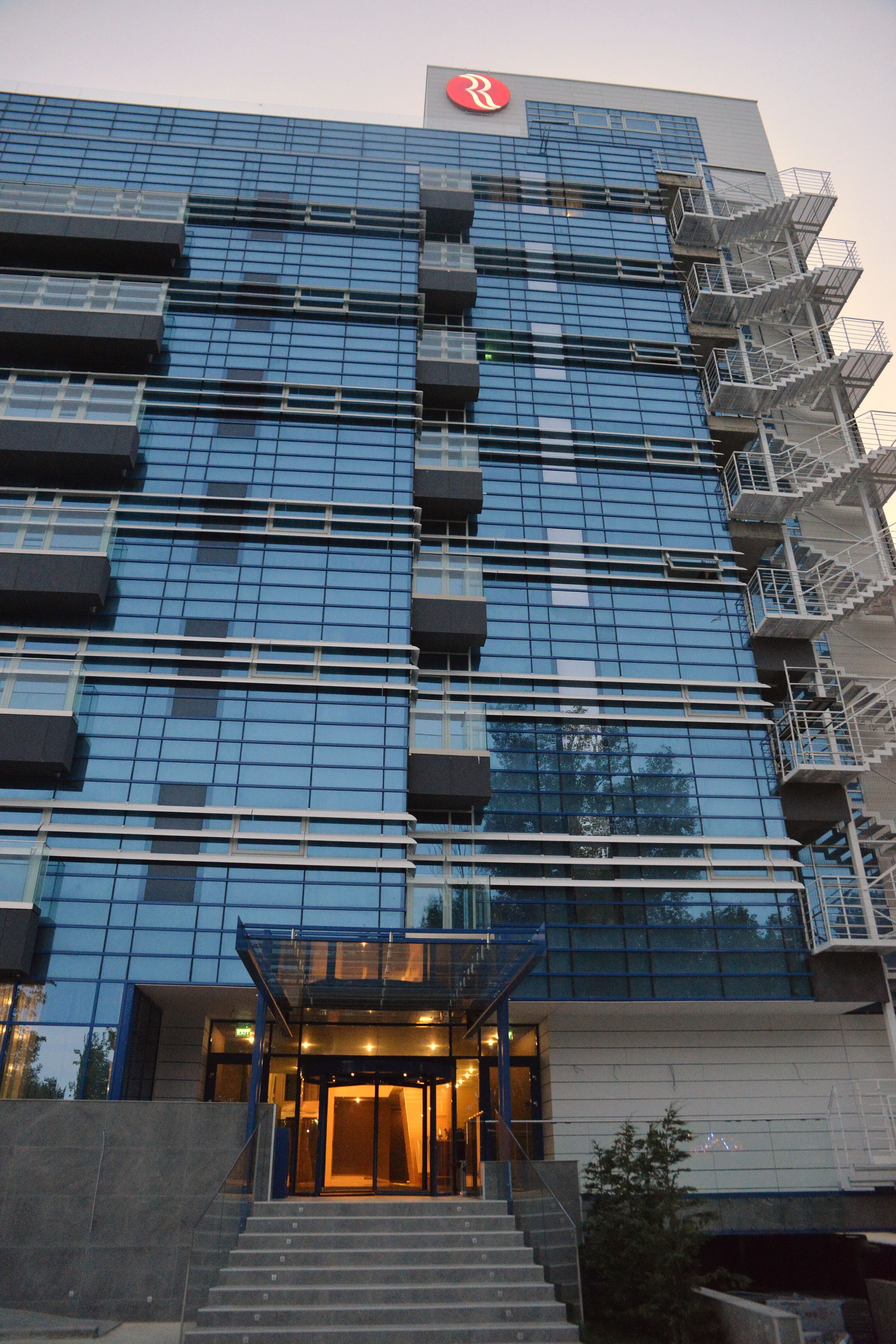 A modern building with a glass facade, a prominent logo at the top, and a set of stairs leading to the entrance.
