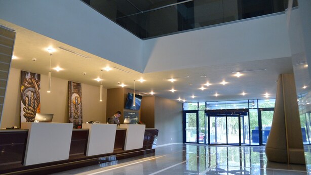 A modern reception area with a glass ceiling, a reception desk, and a large window providing a view of the outdoors. - Ramada by Wyndham Constanta (Constanta)