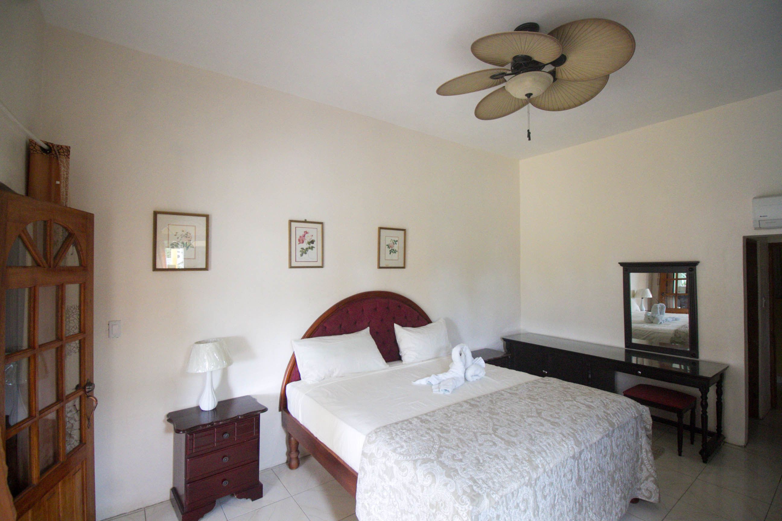 Ein Hotelzimmer mit Bett, Schreibtisch, Stuhl, Spiegel und Deckenventilator.