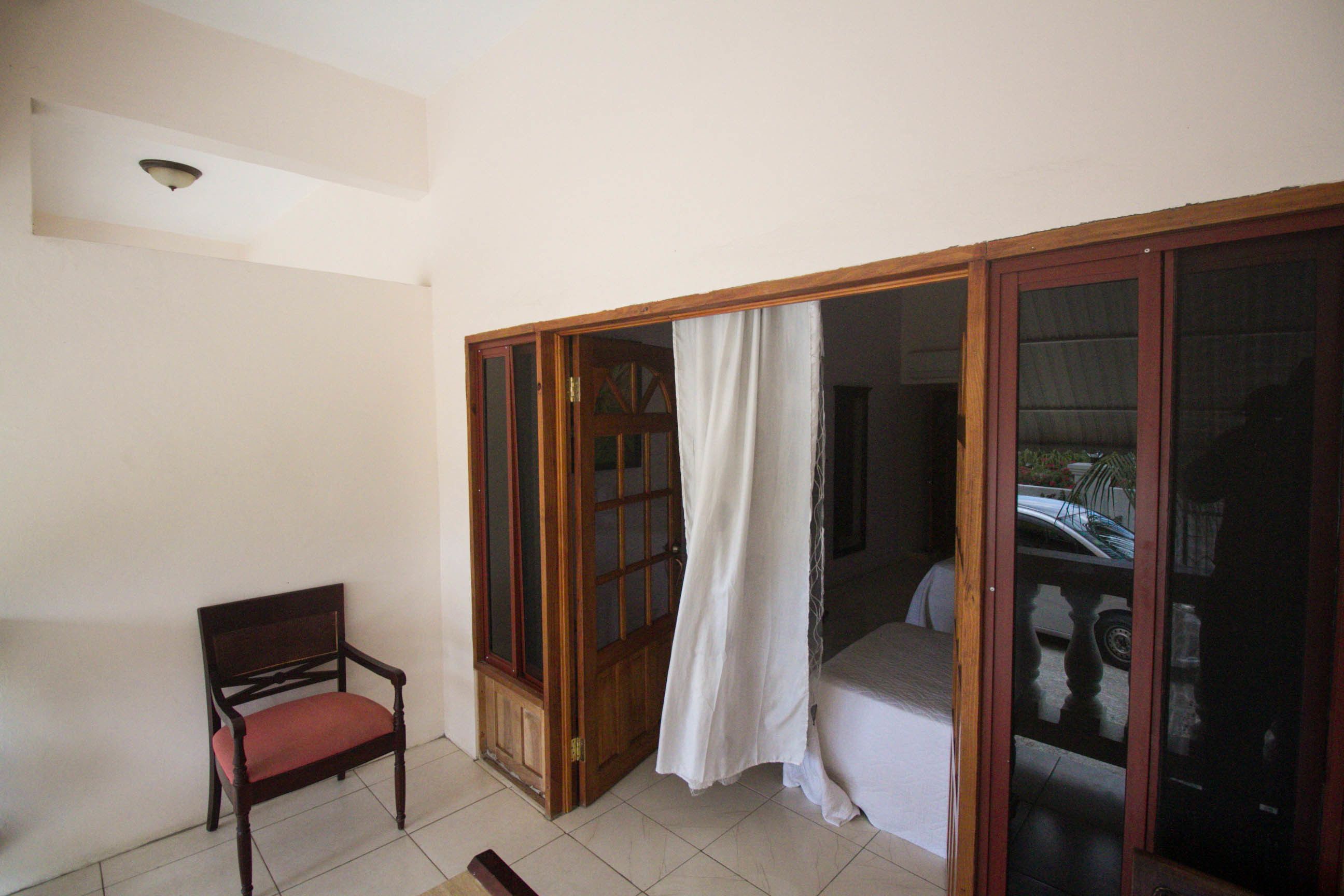 Une pièce avec une chaise en bois, une porte-fenêtre coulissante et un rideau blanc.