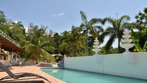 A swimming pool with a tiled deck, lounge chairs, and a white wall with a decorative fountain. - Chateau Margarite Hotel (Montego Bay)