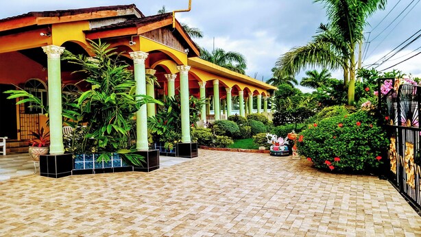 A covered outdoor area with tiled flooring, columns, and potted plants. - Chateau Margarite Hotel (Montego Bay)