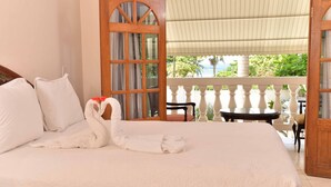 A hotel room with a bed, a balcony with a table and chairs, and a view of greenery and a body of water. - Chateau Margarite Hotel (Montego Bay)
