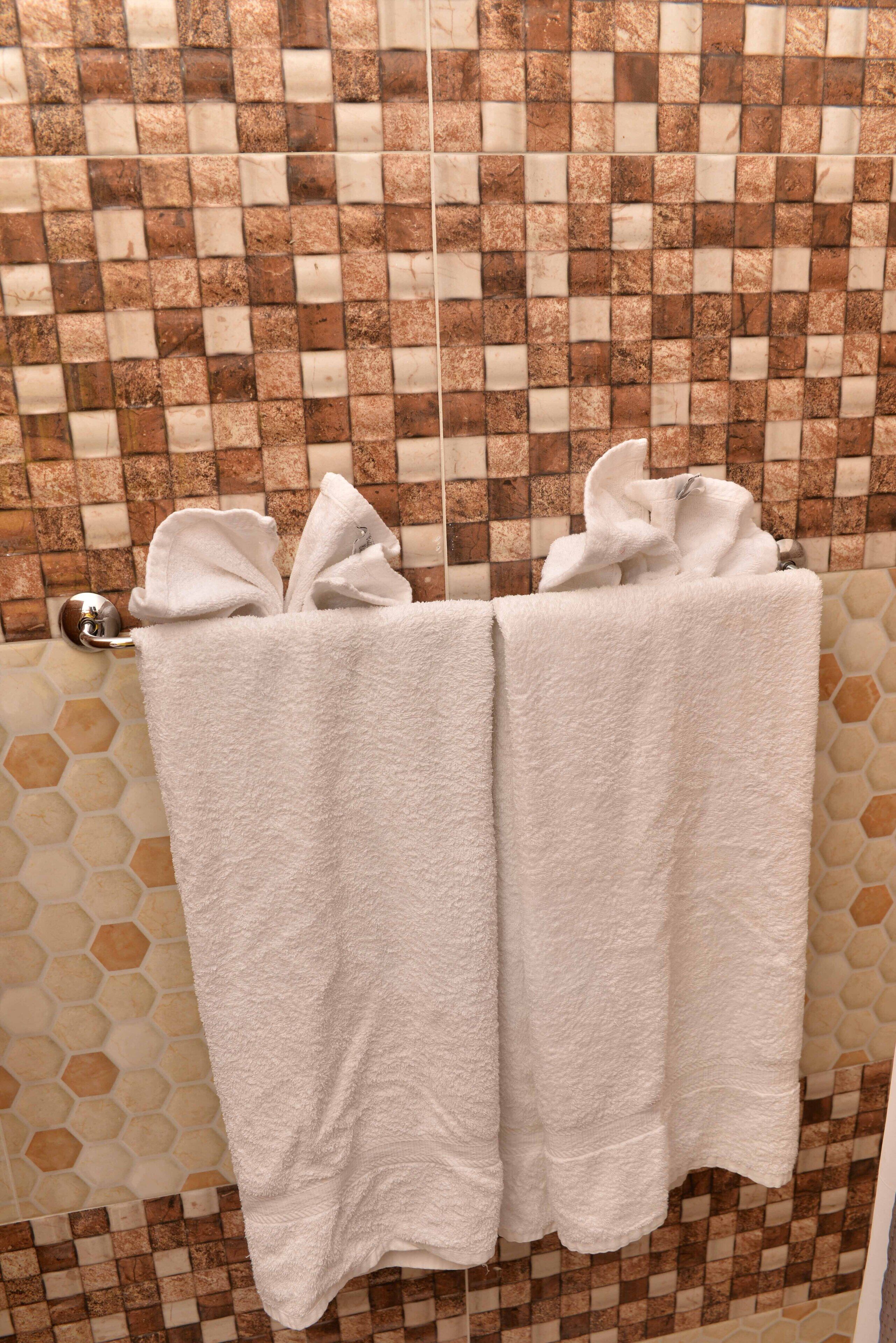 A bathroom with a tiled wall and a towel rack holding two white towels.