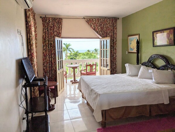 Habitación de hotel con cama, televisor, balcón con mesa y sillas, y vistas al exterior.