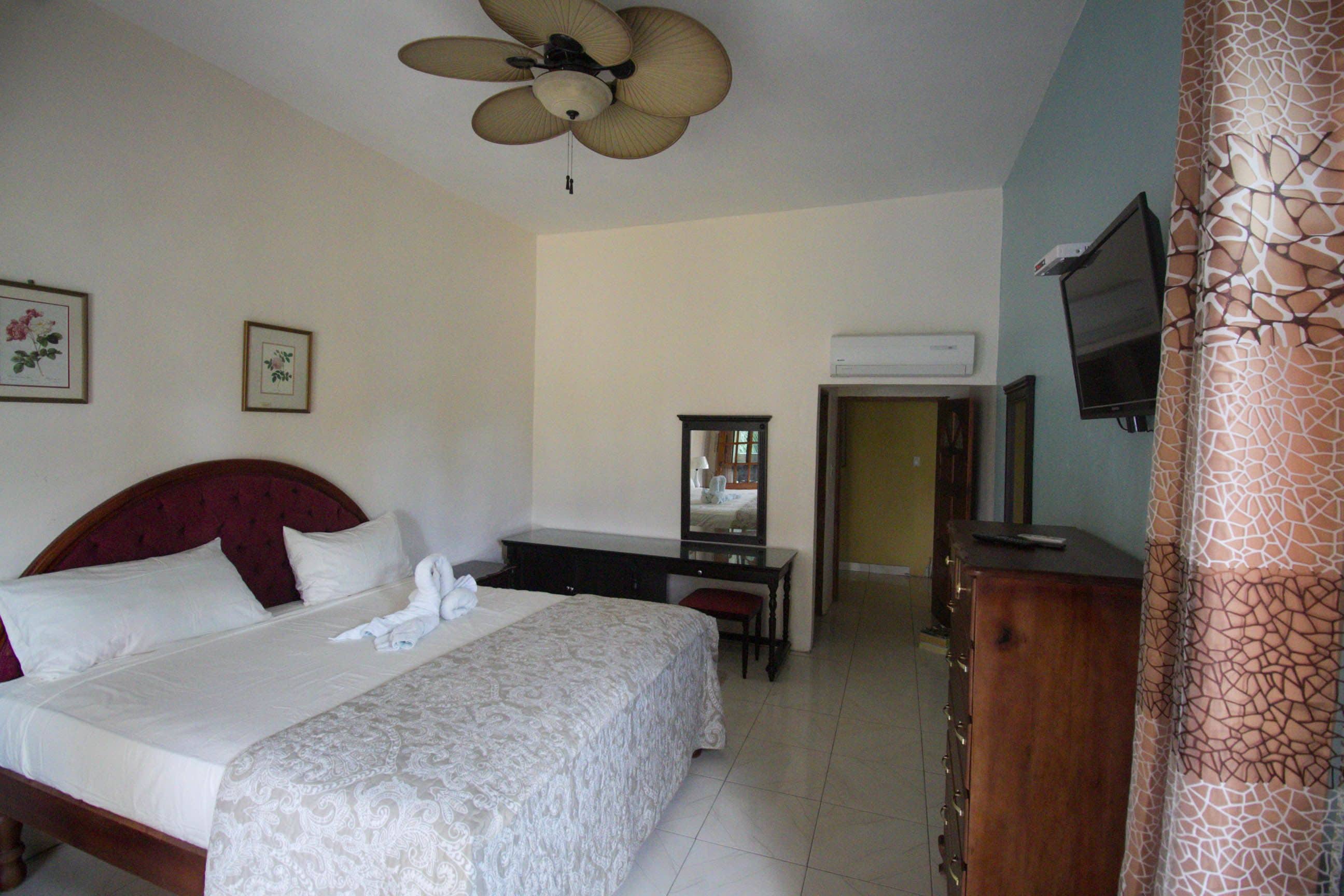 A hotel room with a bed, a desk, a television, and a ceiling fan.