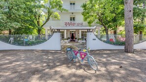 Entrada de hotel con una bicicleta estacionada frente, rodeada de árboles y un camino de grava.