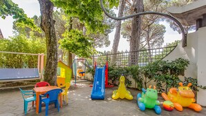 Un parque infantil con sillas de plástico de colores, un tobogán y juguetes inflables con forma de animales.