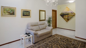 Un saló amb un sofà beix, una taula petita blanca, un lampadari i un gran moixinet estampat.
