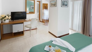 Habitació d'hotel amb llit, escriptori amb televisió, cadira, nevera petita, tassa de cafè i safata amb galetes.