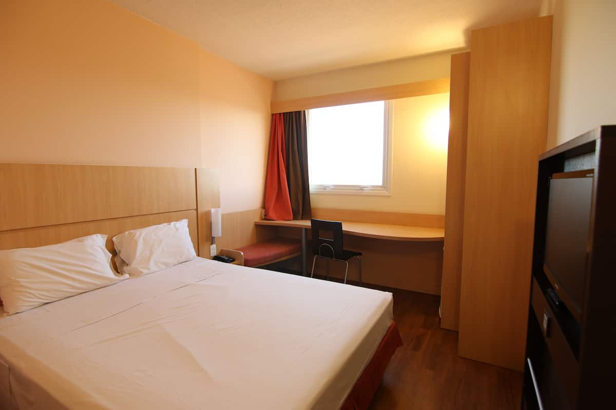A hotel room with a bed, desk, chair, and TV.