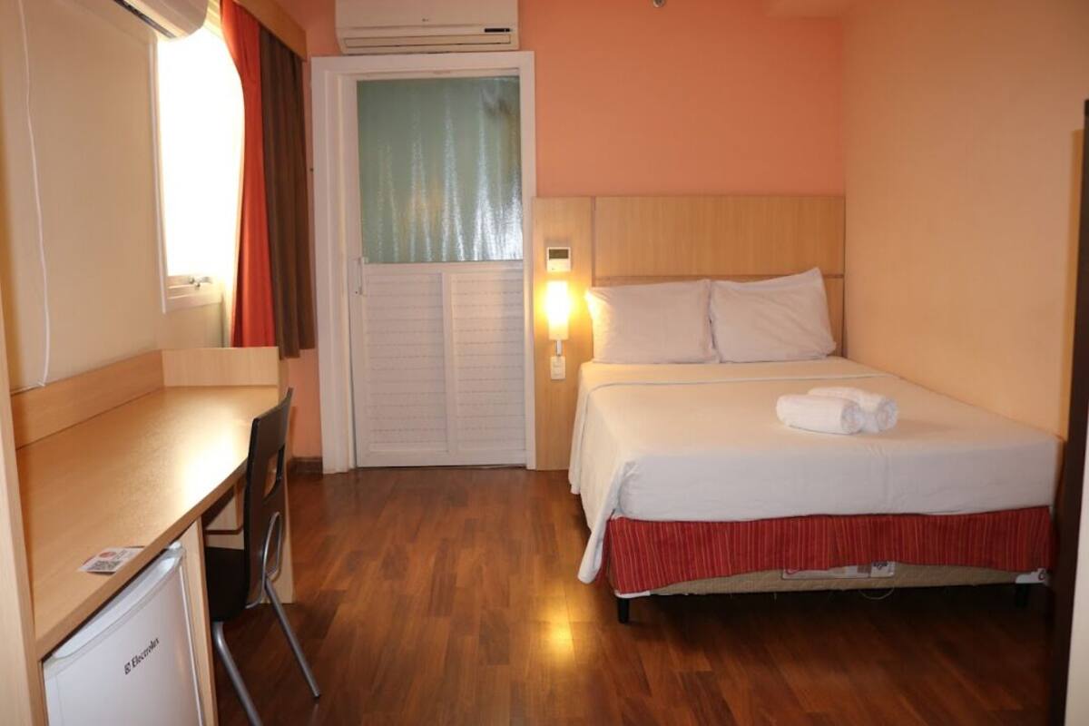 A hotel room with a bed, a desk, a chair, a wardrobe, and a window with curtains.
