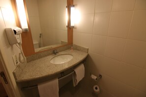 Un baño con lavamanos, espejo, toallero y secador de pelo.