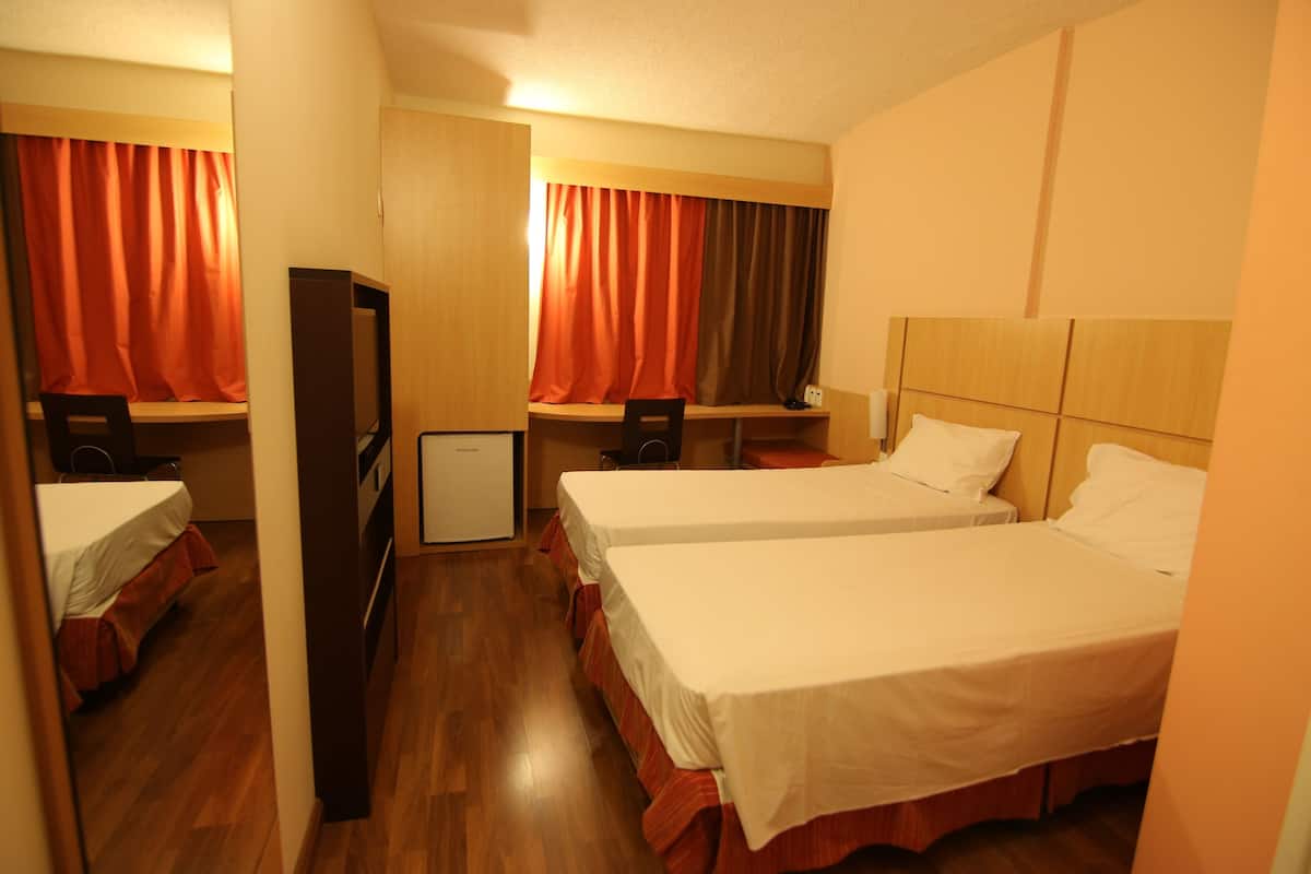 A hotel room with two beds, a desk, a chair, a TV, and a wardrobe.