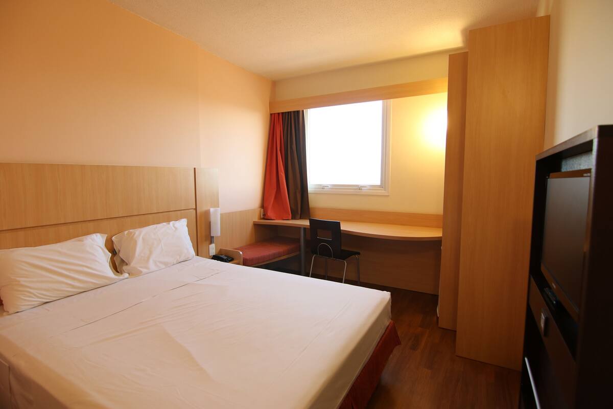 A hotel room with a bed, desk, chair, and TV.