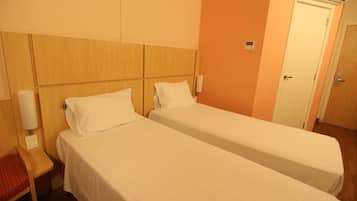 Una habitación de hotel con dos camas individuales, cabecero de madera, unidad de aire acondicionado y una puerta.